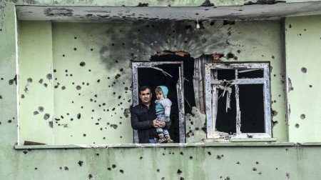 A man holding an infant stands on the balcony of a damaged house, after curfew ended in the southeastern Turkish town of Silopi on January 19, 2016. Turkey is waging an all-out offensive against the separatist Kurdistan Workers' Party (PKK), with military operations backed by curfews aimed at flushing out rebels from several southeastern urban centres.  / AFP / ILYAS AKENGIN