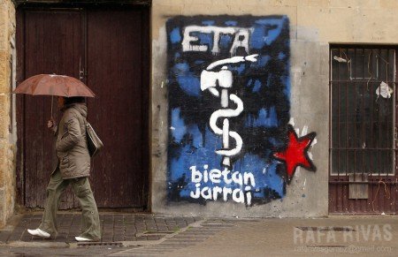 A woman walks past a graffiti representing the pro-independence armed Basque group ETA logo, 23 March 2006 in the northern Spanish village of Alsasua, Navarra province. PHOTO RAFA RIVAS